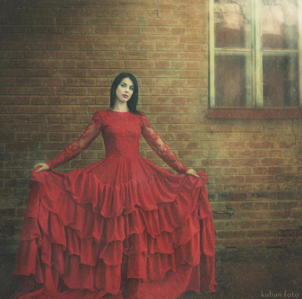 Junge Frau im roten Ballkleid vor einem Haus